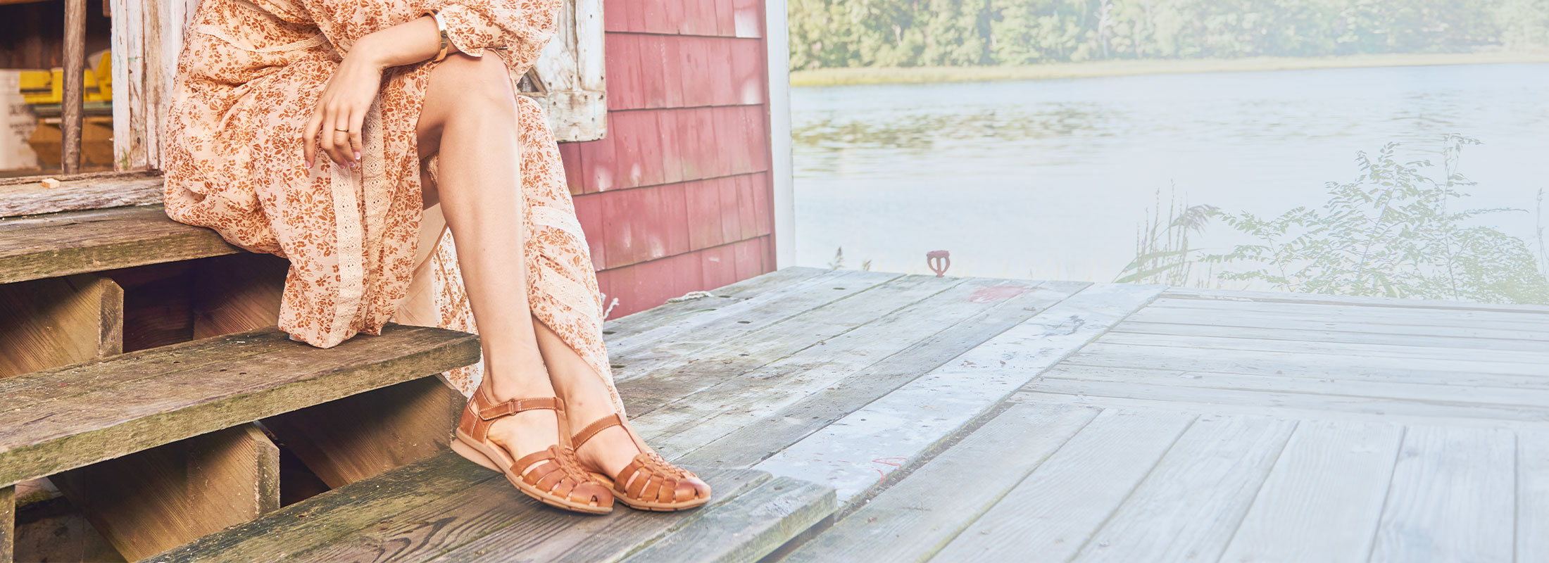 A woman sitting on a dock wearing the Persa sandals in tan.
